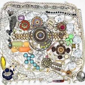 May include: A collection of vintage jewelry, including necklaces, bracelets, rings, and brooches. The pieces feature a variety of colors, including silver, gold, turquoise, red, and green. Many items are adorned with rhinestones and gemstones.