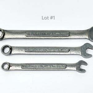 May include: Three silver-colored metal combination wrenches of varying sizes arranged horizontally. Each tool features a box end and an open end, with the text "FORGED IN U.S.A." and specific size markings embossed on the handle. The image includes the text "Lot #1".