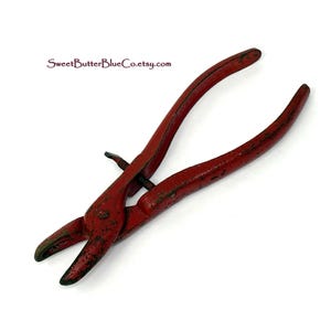 May include: A vintage pair of red pliers with a curved handle and a pointed tip. The pliers have a distressed finish, showing signs of wear and age. The text "SweetButterBlueCo.etsy.com" is visible.