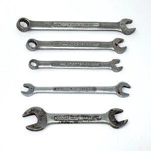 May include: A set of five silver-colored metal Craftsman wrenches arranged horizontally. Four wrenches are combination style with an open end and a box end, while the bottom wrench is a double open-ended style. Each tool features embossed text.