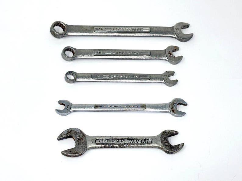 May include: A set of five silver-colored metal Craftsman wrenches arranged horizontally. Four wrenches are combination style with an open end and a box end, while the bottom wrench is a double open-ended style. Each tool features embossed text.