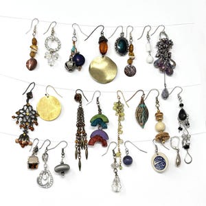 May include: A collection of assorted dangle earrings, each with unique designs and materials. The earrings feature various colors, including gold, silver, brown, blue, and green. Some earrings have beads, charms, and geometric shapes, while others have a more organic, natural look.