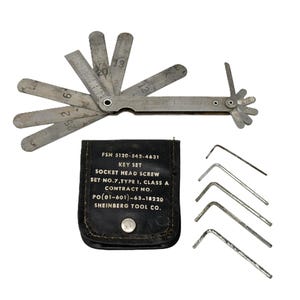 May include: A set of vintage metal tools, including a feeler gauge with measurements in inches, a key set, and a small black pouch with text. The tools are arranged on a white background.