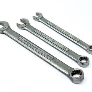 May include: Three silver-colored metal combination wrenches arranged diagonally. Each tool features an open-end on one side and a box-end on the other, with the brand name Craftsman and size markings 3/8, 5/16, and 1/4 inches embossed on the shafts.