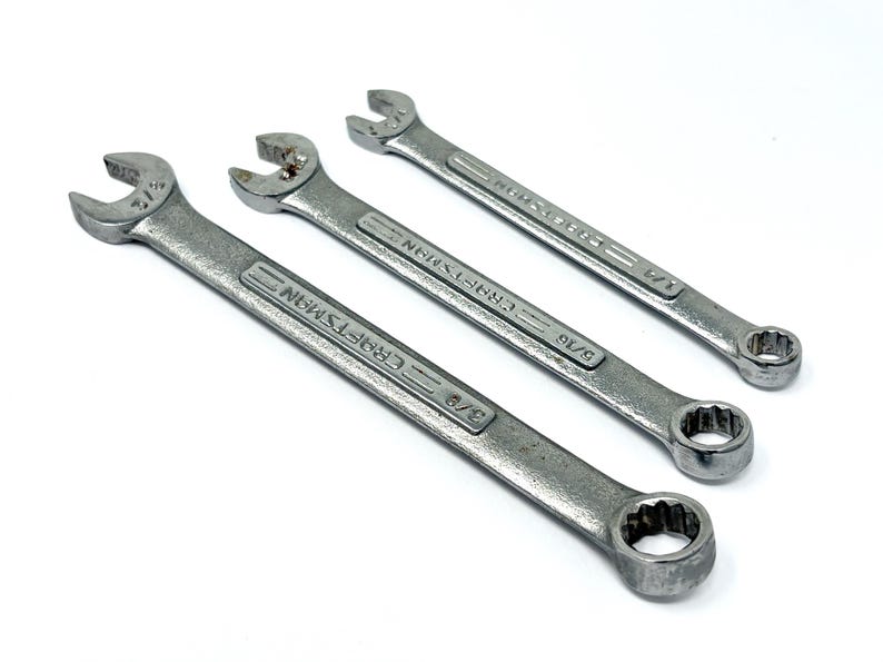 May include: Three silver-colored metal combination wrenches arranged diagonally. Each tool features an open-end on one side and a box-end on the other, with the brand name Craftsman and size markings 3/8, 5/16, and 1/4 inches embossed on the shafts.