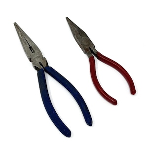 May include: Two needle-nose pliers with metal jaws and curved handles. One has blue handles, the other red. The tools are designed for gripping, bending, and cutting wires and small objects. They are set against a white background.