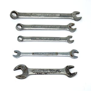 May include: Five Craftsman wrenches of varying sizes are arranged on a white background. The wrenches are silver-colored, with the Craftsman logo and size markings visible. The sizes include 3/8, 7/16, 1/2, 5/16, and 3/4 inch.