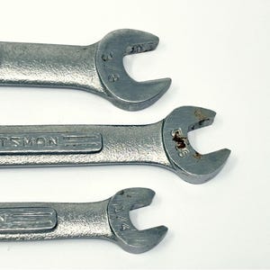 May include: Three silver-colored metal Craftsman wrenches arranged horizontally. The top wrench is marked 3/8 inch, the middle wrench is marked 5/16 inch with visible rust, and the bottom wrench is marked 1/4 inch. Each tool features an open-end design.