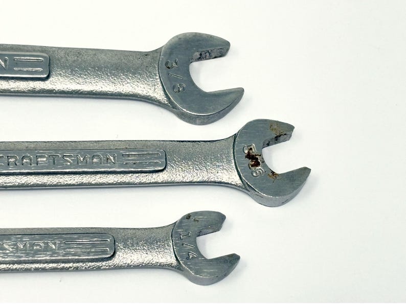 May include: Three silver-colored metal Craftsman wrenches arranged horizontally. The top wrench is marked 3/8 inch, the middle wrench is marked 5/16 inch with visible rust, and the bottom wrench is marked 1/4 inch. Each tool features an open-end design.