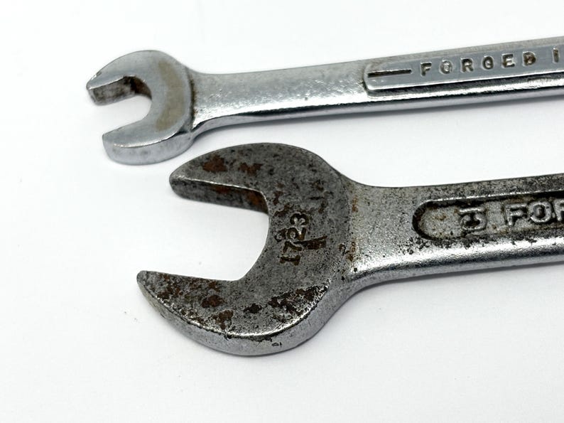 May include: Two silver-colored metal wrenches with open-ended heads. The top wrench has a smooth, polished finish with the text FORGED IN visible. The bottom wrench has a weathered, textured surface with rust spots and the number 1723 stamped on it.