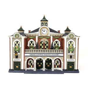 May include: A ceramic miniature of Grand Central Railway Station. The building features a clock tower, arched doorways, and decorative wreaths. The facade is brick and gray with green accents. The text "GRAND CENTRAL RAILWAY STATION" is displayed on the front.
