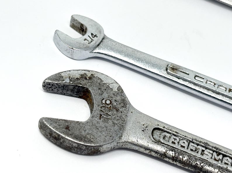 May include: Two silver-colored metal wrenches with open ends. The top wrench is marked 1/4 inch and the bottom wrench is marked 7/16 inch. Both wrenches feature the brand name Craftsman embossed on the handle. The bottom wrench shows signs of wear.