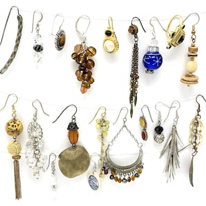 May include: A collection of various earrings hanging against a white background. The earrings feature diverse designs, including beaded, dangling, and stud styles, with a range of colors and materials like metal, beads, and gemstones. The earrings are displayed on a thin white string.