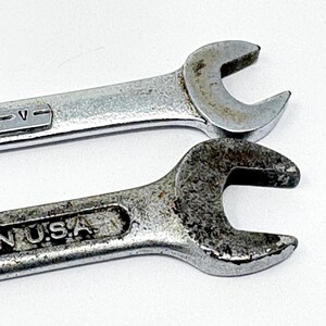 May include: Two silver-colored metal open-end wrenches with visible signs of wear and oxidation. The top wrench features the text U.S.A. V, while the bottom wrench displays the text ED IN U.S.A. embossed on the handle surface.