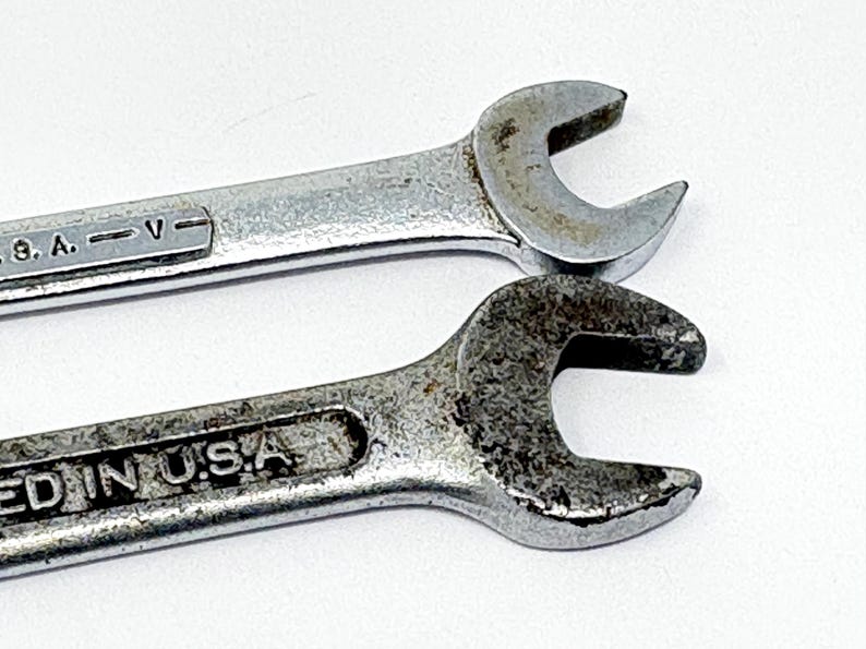 May include: Two silver-colored metal open-end wrenches with visible signs of wear and oxidation. The top wrench features the text U.S.A. V, while the bottom wrench displays the text ED IN U.S.A. embossed on the handle surface.