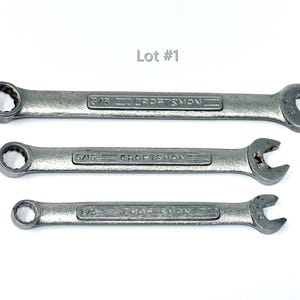 May include: Three silver-colored metal Craftsman combination wrenches arranged horizontally. The wrenches are labeled 3/8 inch, 5/16 inch, and 1/4 inch. The text Lot #1 is positioned above the wrenches. Each tool features a box end and an open end.