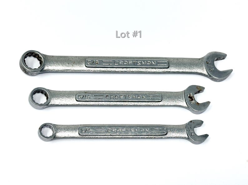 May include: Three silver-colored metal Craftsman combination wrenches arranged horizontally. The wrenches are labeled 3/8 inch, 5/16 inch, and 1/4 inch. The text Lot #1 is positioned above the wrenches. Each tool features a box end and an open end.