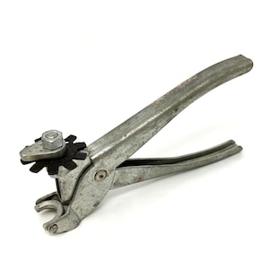 May include: A vintage metal tool with a lever handle and a gear-like component. The tool has a silver finish with signs of wear and tear, suggesting it's been used. The design includes a nut and bolt for adjustment, and a curved end.