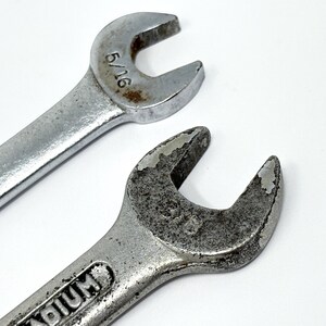 May include: Two silver-colored metal wrenches with open-ended heads. The top wrench is marked 5/16 inches. The bottom wrench shows signs of wear and oxidation on the metal surface, with the word vanadium partially visible on the handle.