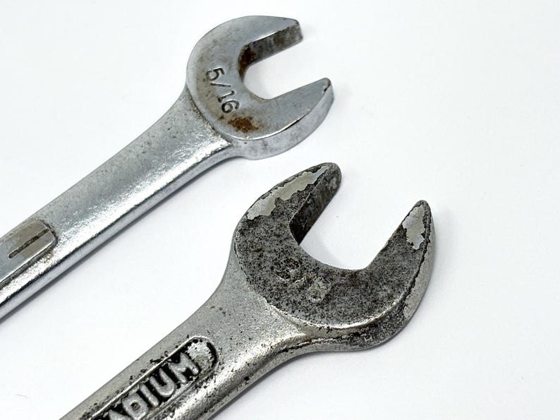 May include: Two silver-colored metal wrenches with open-ended heads. The top wrench is marked 5/16 inches. The bottom wrench shows signs of wear and oxidation on the metal surface, with the word vanadium partially visible on the handle.