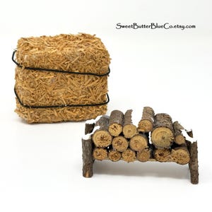May include: A miniature hay bale tied with black twine and a small wooden log rack with faux snow. The log rack is filled with cut logs. The items are set against a white background.