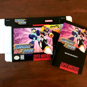 Puede incluir: Una caja de juego de Super Nintendo y un folleto de instrucciones para "Mega Man & Bass". La caja es negra con arte del juego de dos personajes en poses de acción. El folleto de instrucciones también es negro con el título del juego y arte de personajes.