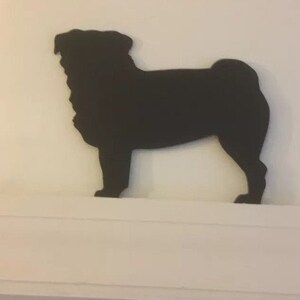 Op de afbeelding: Zwarte silhouet van een mops, staand op een wit rek.