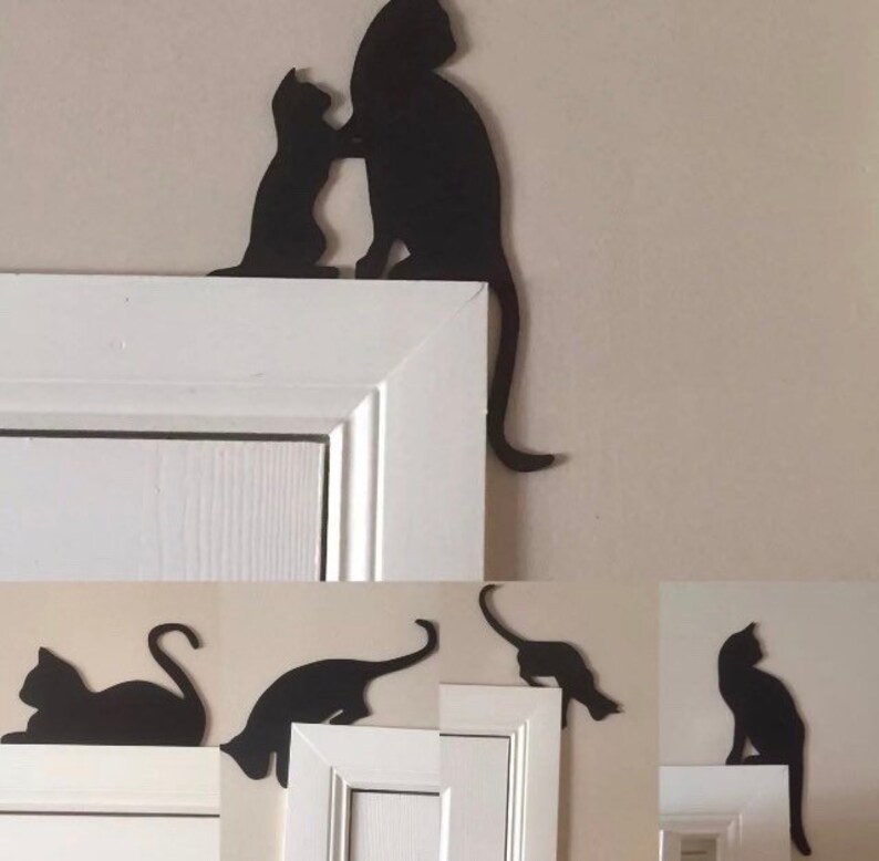 Op de afbeelding: Zwarte silhouetten van katten op een wit deurkozijn. De katten zijn in verschillende poses, waaronder zittend, staand en springend. De silhouetten zijn uit metaal geknipt en zijn met lijm aan het deurkozijn bevestigd.