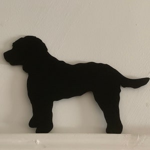 May include: Black silhouette of a dog standing on a white surface. The dog is facing to the left and has a long tail.