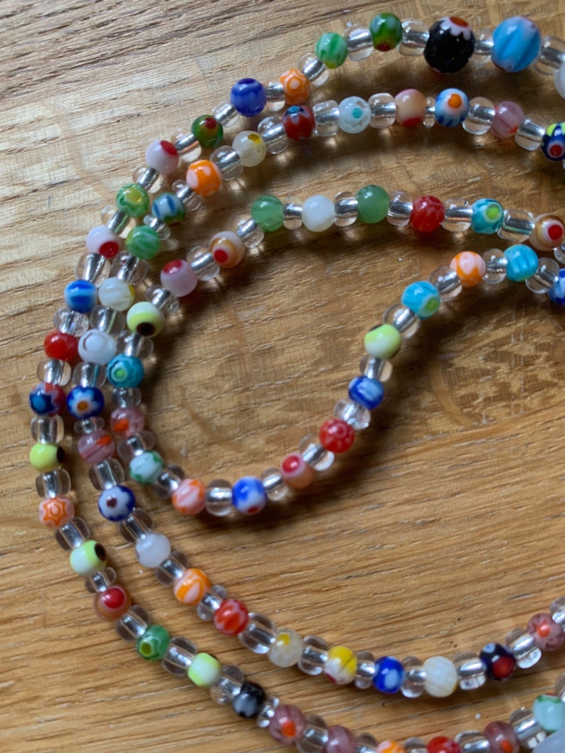 May include: Multicolored glass bead necklace with clear beads. The necklace is made of small, round beads with various patterns and colors, including red, blue, green, yellow, and white.