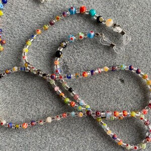 May include: A colorful beaded glasses chain with clear beads and small, colorful glass beads with floral patterns. The chain has two clear plastic clasps for attaching to glasses.