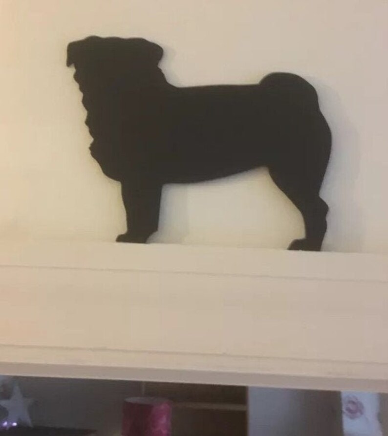 Op de afbeelding: Zwarte silhouet van een mops, staand op een wit rek.
