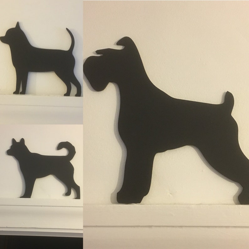 Op de afbeelding: Drie zwarte silhouet-uitsnijdingen van honden. De silhouetten zijn van een chihuahua, een schnauzer en een kleine terri&euml;r. De silhouetten zijn gemonteerd op een witte muur.