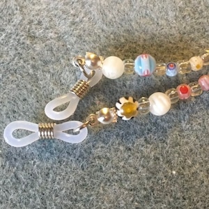 May include: A pair of clear plastic eyeglass holders with silver metal spring clips and a beaded chain with white, pink, blue, and yellow beads.