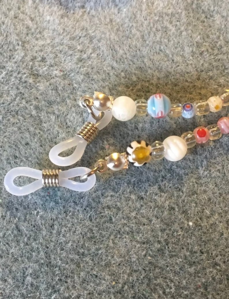 May include: A pair of clear plastic eyeglass holders with silver metal spring clips and a beaded chain with white, pink, blue, and yellow beads.