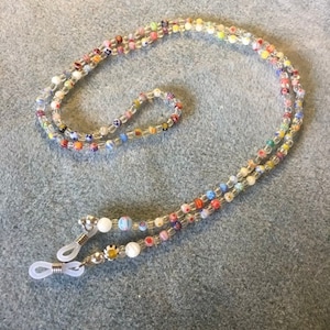 May include: A colorful beaded eyeglass chain with clear beads and small, colorful patterned beads. The chain has two silver metal clasps with clear plastic loops on each end.