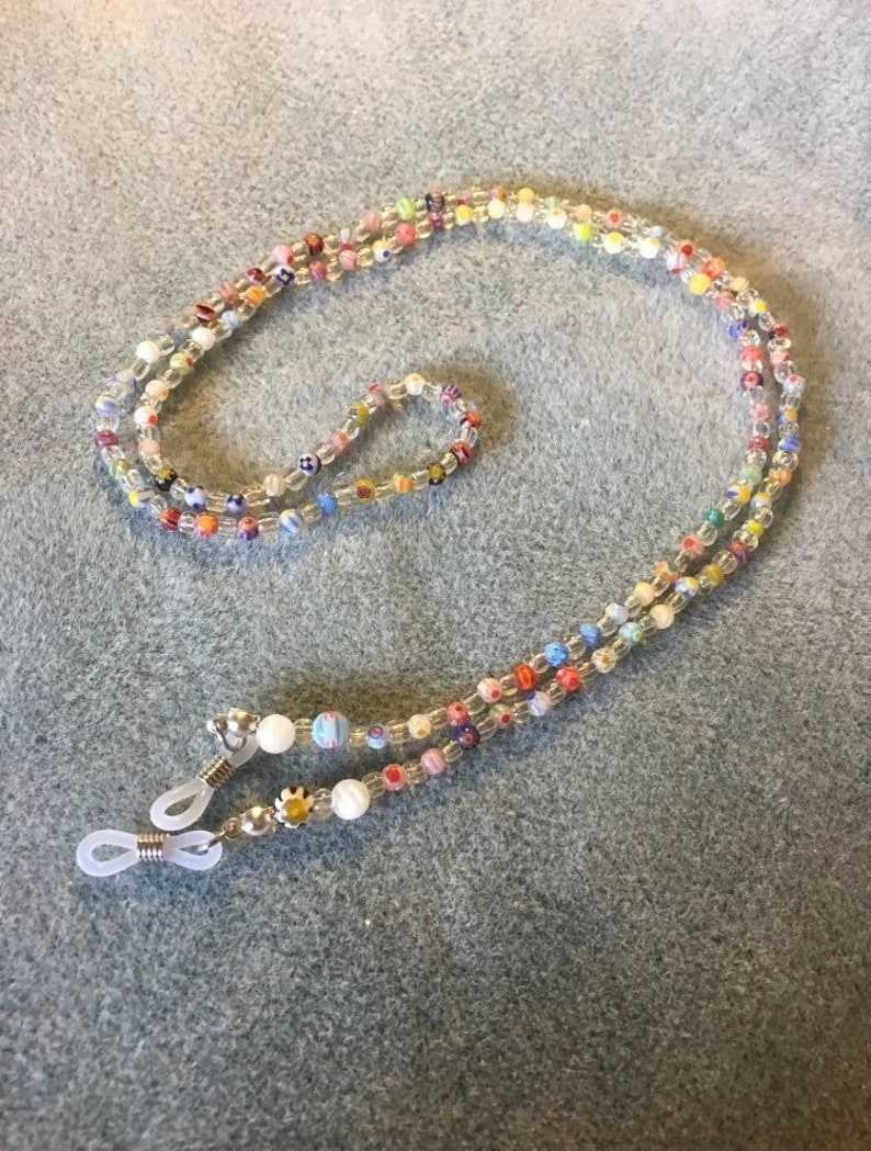 May include: A colorful beaded eyeglass chain with clear beads and small, colorful patterned beads. The chain has two silver metal clasps with clear plastic loops on each end.