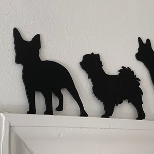 Op de afbeelding: Drie zwarte silhouet-uitsnijdingen van honden op een witte muur. De honden zijn een Franse Bulldog, een Shih Tzu en een Jack Russell Terrier.
