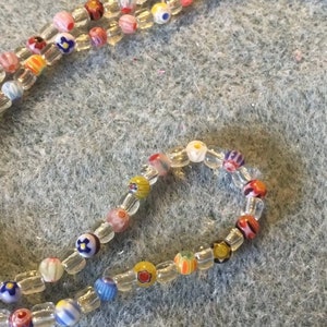 May include: A colorful beaded necklace with small, clear beads and colorful glass beads with various patterns. The beads are strung on a clear thread.