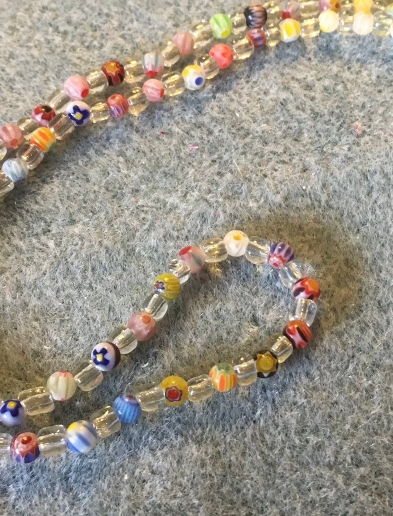 May include: A colorful beaded necklace with small, clear beads and colorful glass beads with various patterns. The beads are strung on a clear thread.