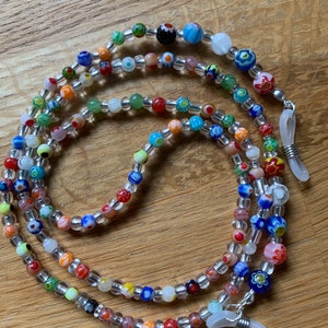 May include: Multicolored beaded eyeglass chain with clear beads and silver clasps. The chain is made of small, round beads with various patterns and colors, including red, blue, green, yellow, and white.