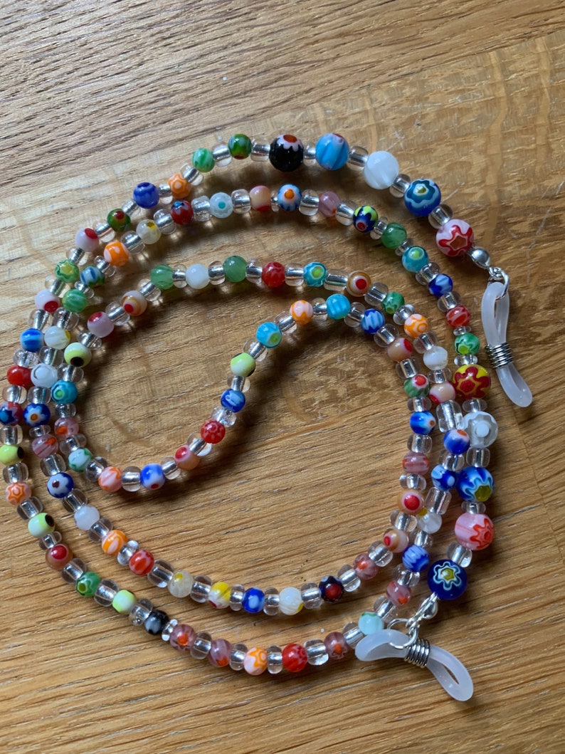 May include: Multicolored beaded eyeglass chain with clear beads and silver clasps. The chain is made of small, round beads with various patterns and colors, including red, blue, green, yellow, and white.