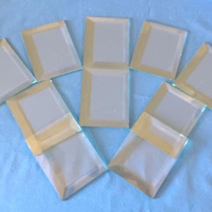 May include: A set of eight small, rectangular, beveled-edge mirrors with a gold trim. The mirrors are arranged in a fan shape on a light blue surface.