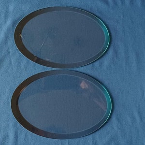 May include: Two clear glass oval-shaped serving trays with black rims. The trays are on a blue surface.
