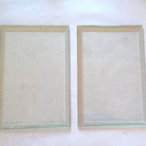 May include: Two rectangular glass panels with a light-colored border are displayed side by side against a white background. One panel has a small hole near the top. The glass is transparent.