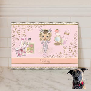 May include: A pink and gold decorative canvas print featuring a cartoon girl surrounded by makeup items. The print includes makeup brushes, eyeshadow palettes, a compact mirror, and lipstick. The name "Lucy" is written across the bottom.