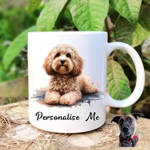 May include: White ceramic mug featuring a watercolor illustration of a light brown Cavapoo dog. The mug has a curved handle and the words "Personalise Me" in black script. The background is blurred with green foliage.