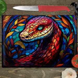 May include: A colourful stained glass style chopping board featuring a red, orange and yellow snake with a blue eye. The snake is curled around a leafy vine with a dark blue background.
