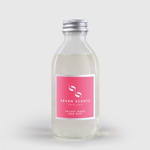 May include: A clear glass bottle with a silver lid and a pink label. The label says "SEVEN SCENTS ENGLAND VELVET ROSE AND OUD".