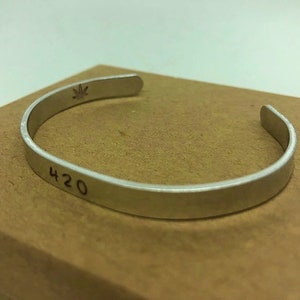 May include: Silver bracelet with a leaf design and the number 420 engraved on it.